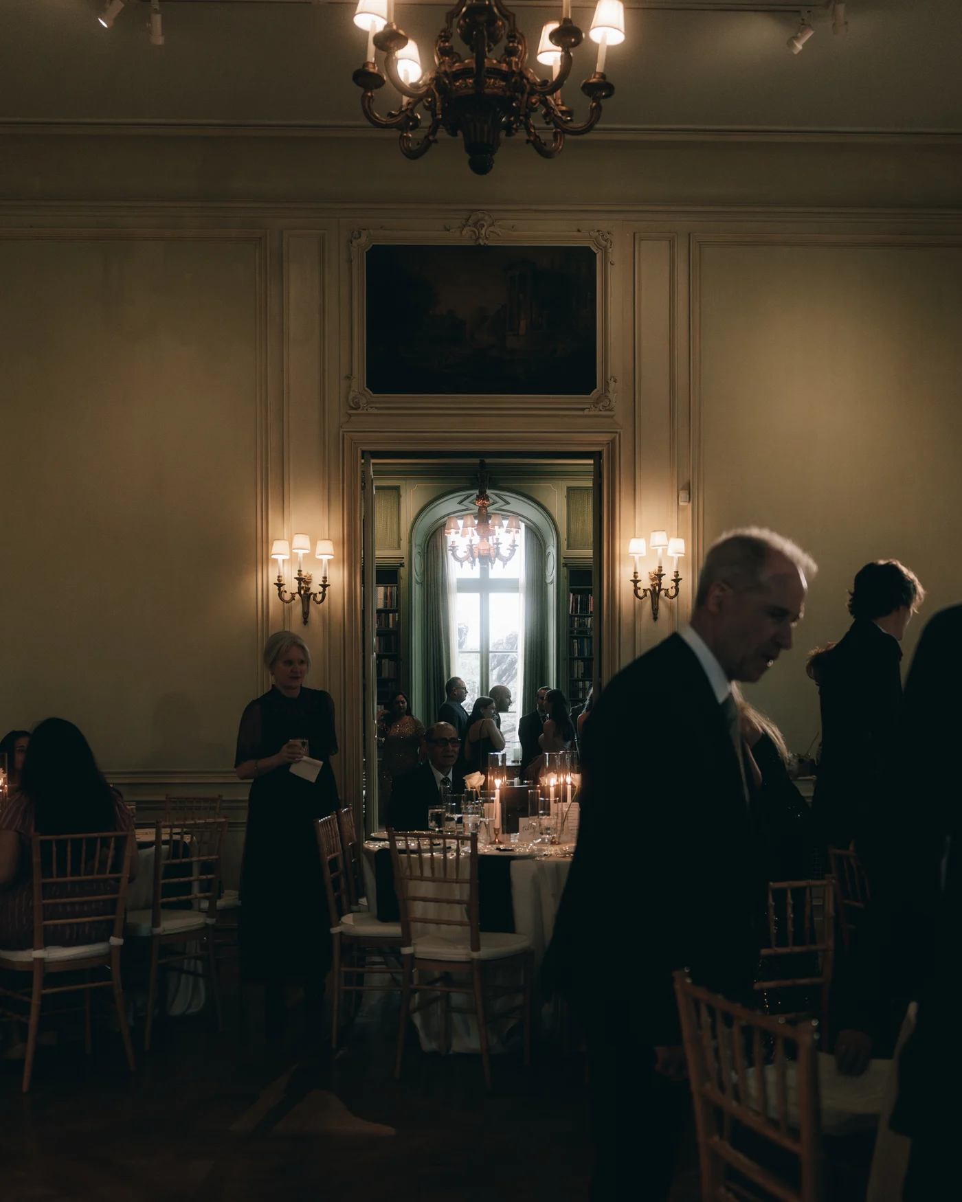 The reception room filling with guests under the chandeliers