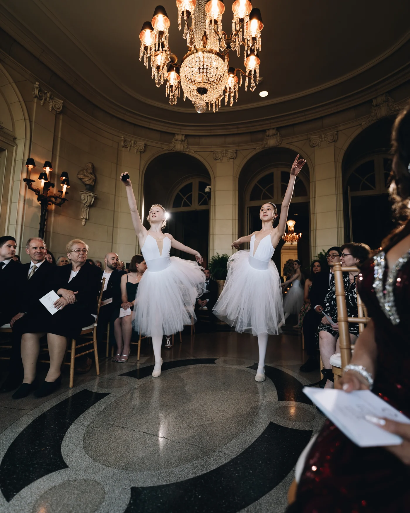 Dancers in white tutus mid performance, the room watching from every side