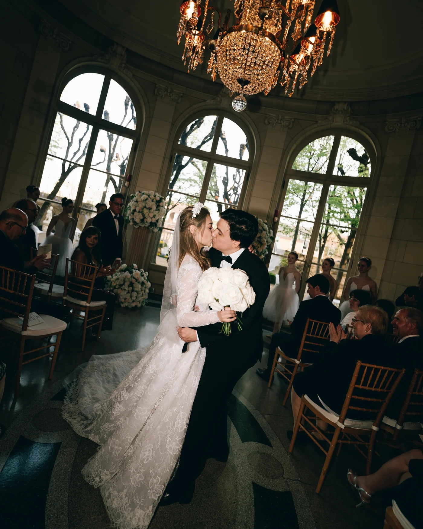 The couple walking through the ballroom beneath the chandeliers