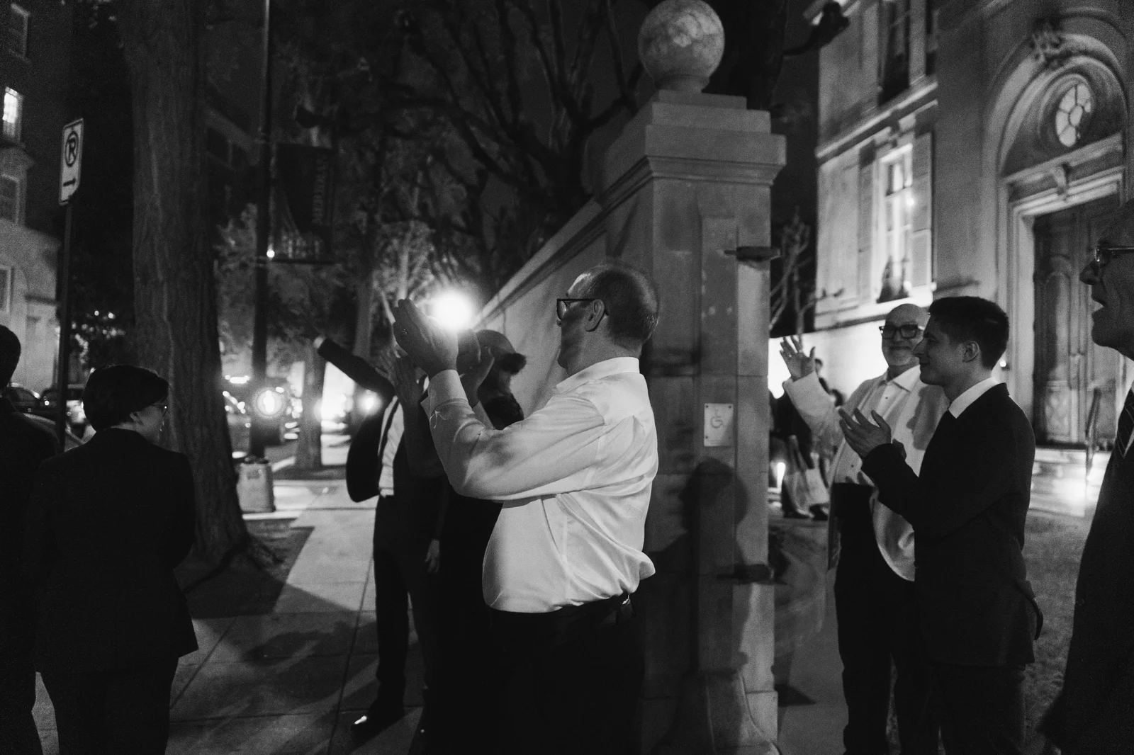 Black and white, the couple holding each other outside at night while the guests look on