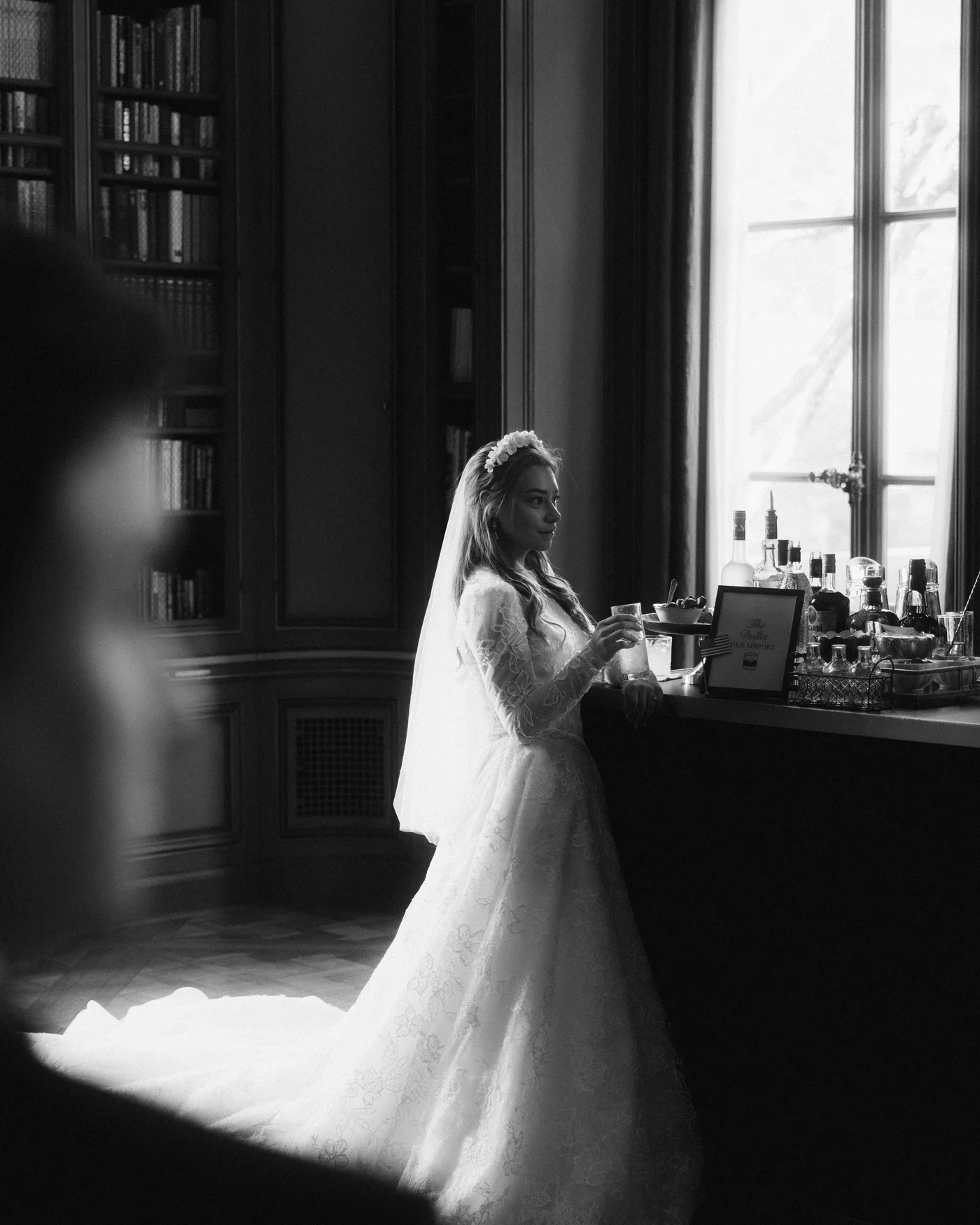 The bride standing at a console against a bright window, her train behind her