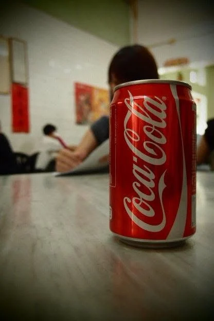 A can of Coca-Cola in sharp focus on a marble table, a diner blurred behind it