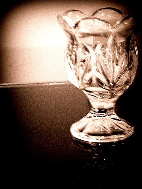 A cut crystal goblet catching light on a dark tabletop, toned sepia with a heavy vignette