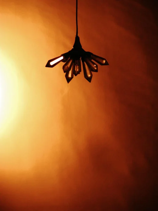 A hanging light fixture with angular bulbs glowing against a wall washed in deep orange