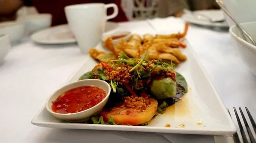 Fried shrimp appetizers with greens, sliced tomato, and a dish of sweet chili sauce on a long white plate