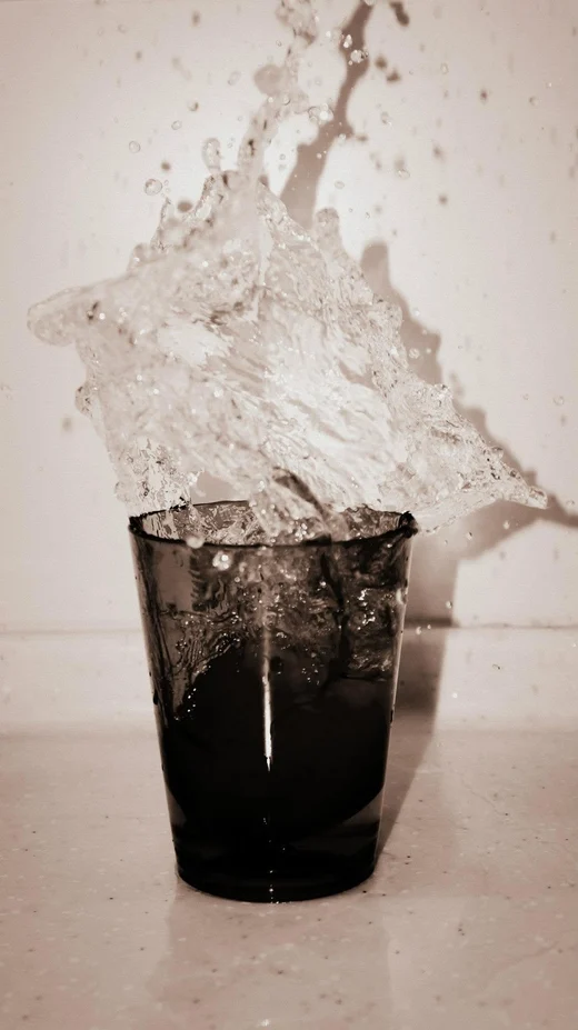 Water frozen mid-splash as it leaps out of a dark tumbler, toned sepia