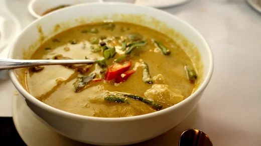 A bowl of green curry flecked with red chili, a spoon buried in the broth
