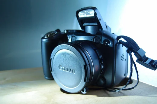 A Canon point and shoot camera with its flash popped up, lit blue from behind