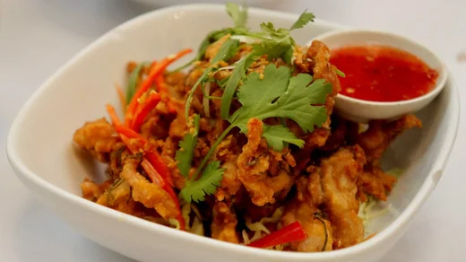 A bowl of crispy fried bites topped with cilantro and chili, sweet chili sauce tucked at the rim