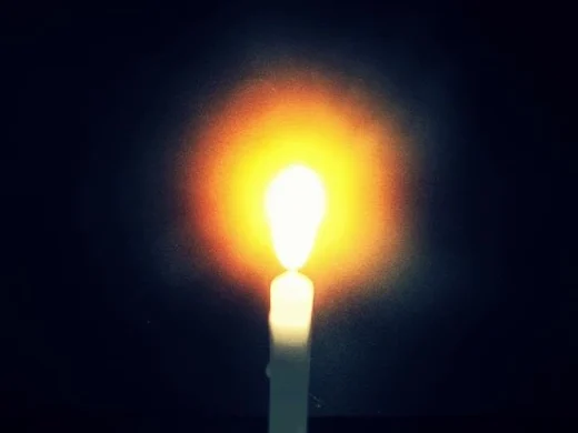 A single candle flame burning against the dark, its halo blooming orange
