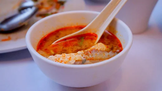 A small bowl of soup rimmed with red chili broth, a long spoon resting inside