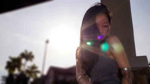 A woman leaning against a column, long hair backlit, the sun flaring across the frame