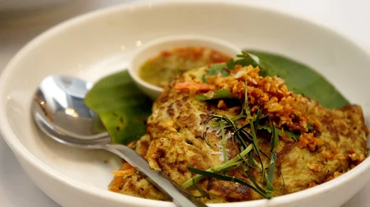An omelette folded over banana leaves with fried garlic and herbs, spoon at the plate's edge