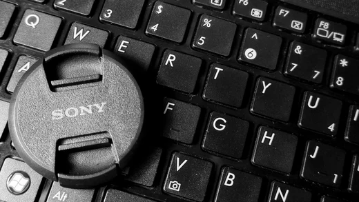 A Sony lens cap resting on the keys of a laptop keyboard, in black and white