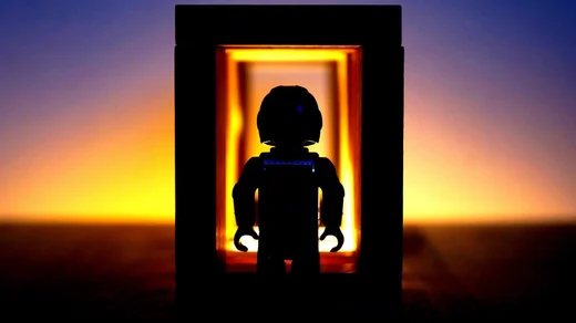 A LEGO figure silhouetted inside a small lit frame against a sunset fading from orange to violet