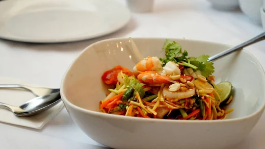 A bowl of shrimp salad with shredded vegetables, peanuts, and lime on a white tablecloth