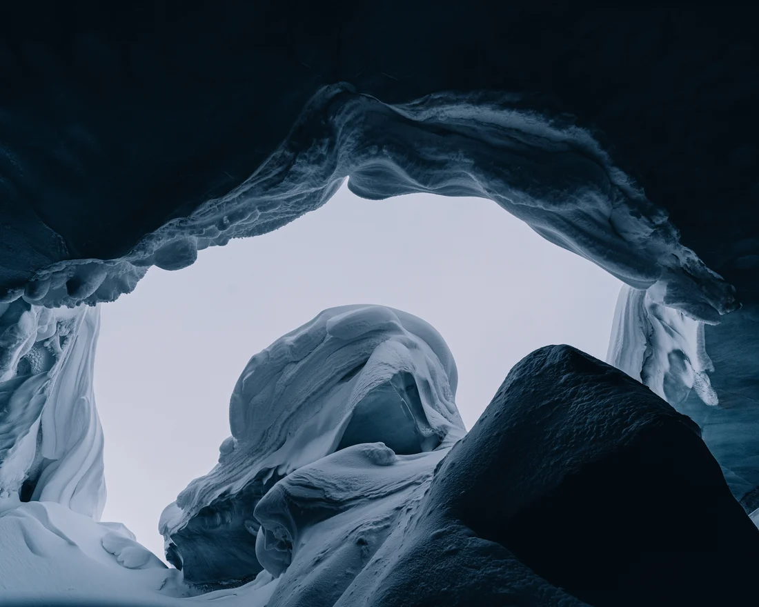 Looking out from inside a glacier cave, the fluted ice roof arching overhead and daylight filling the mouth
