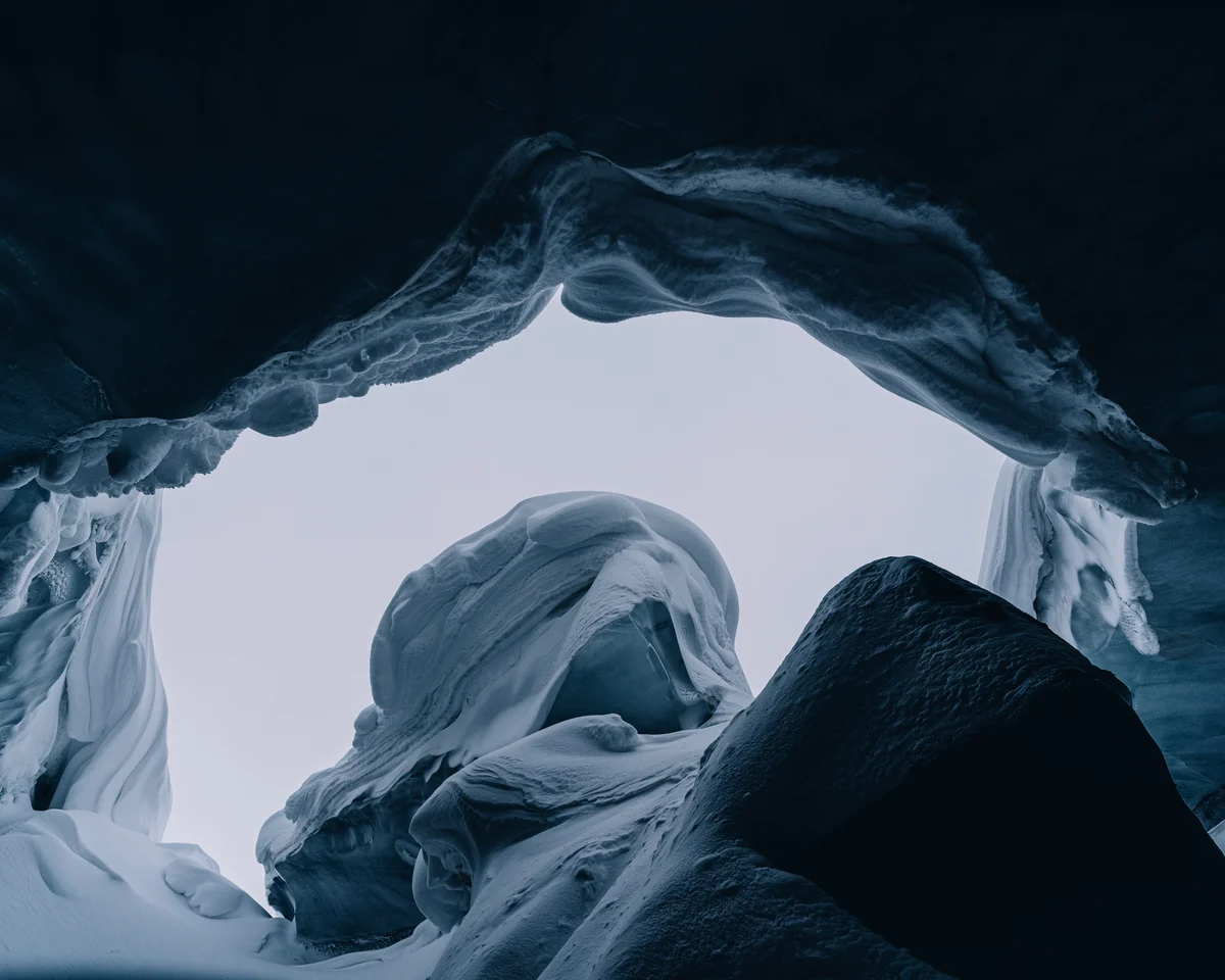 Looking out from inside a glacier cave, the fluted ice roof arching overhead and daylight filling the mouth