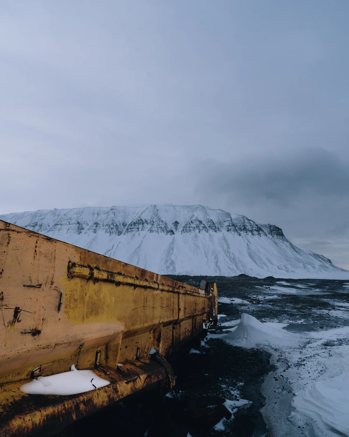 The rusted ochre timber of an abandoned coal works on the shore, a flat-topped snow mountain across the water behind it
