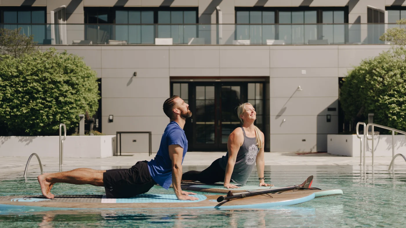 The pair in upward-facing dog on their boards, the glass and stone front of the building behind them