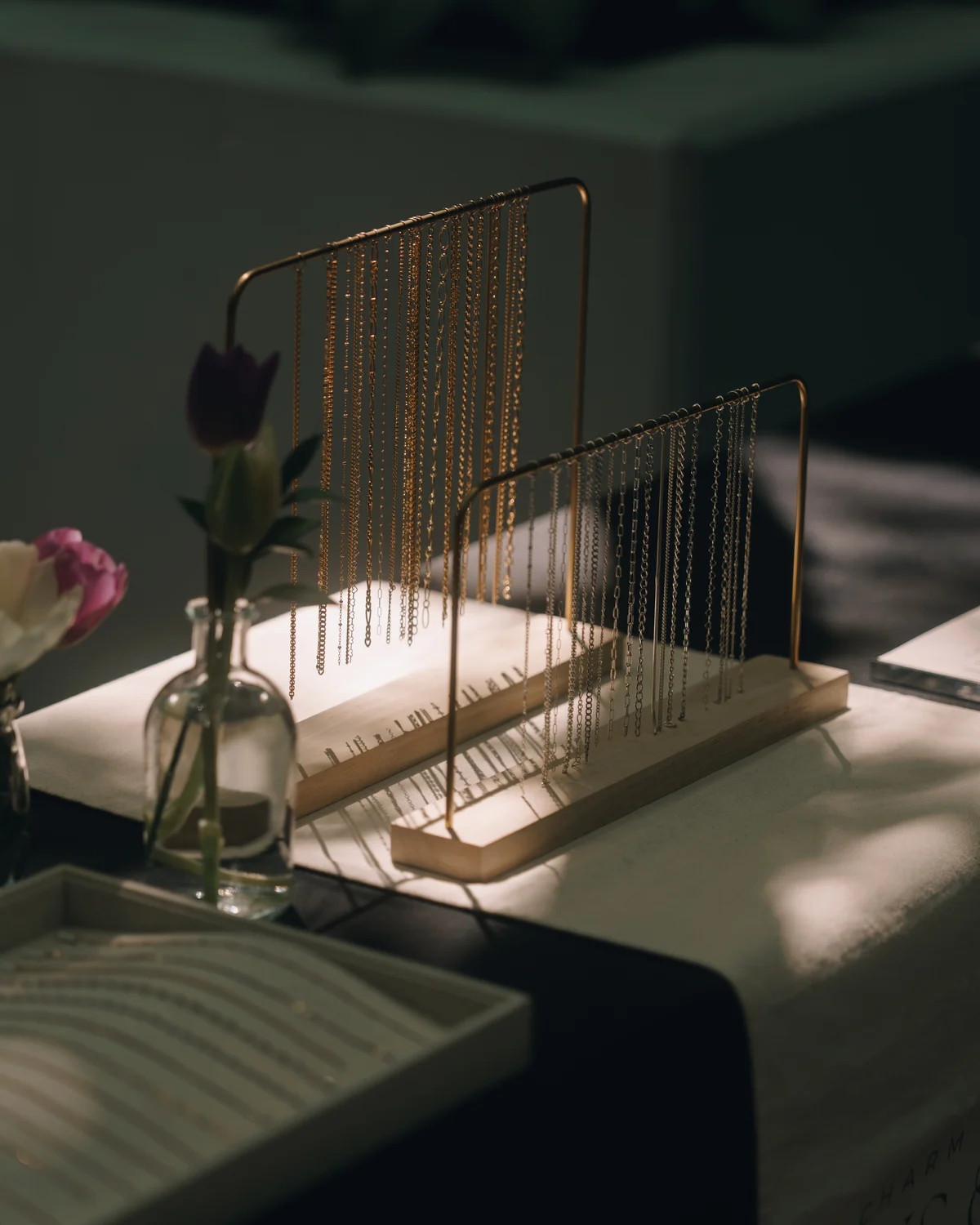 A display stand hung with rows of fine gold chains, a single tulip in a glass bottle beside it