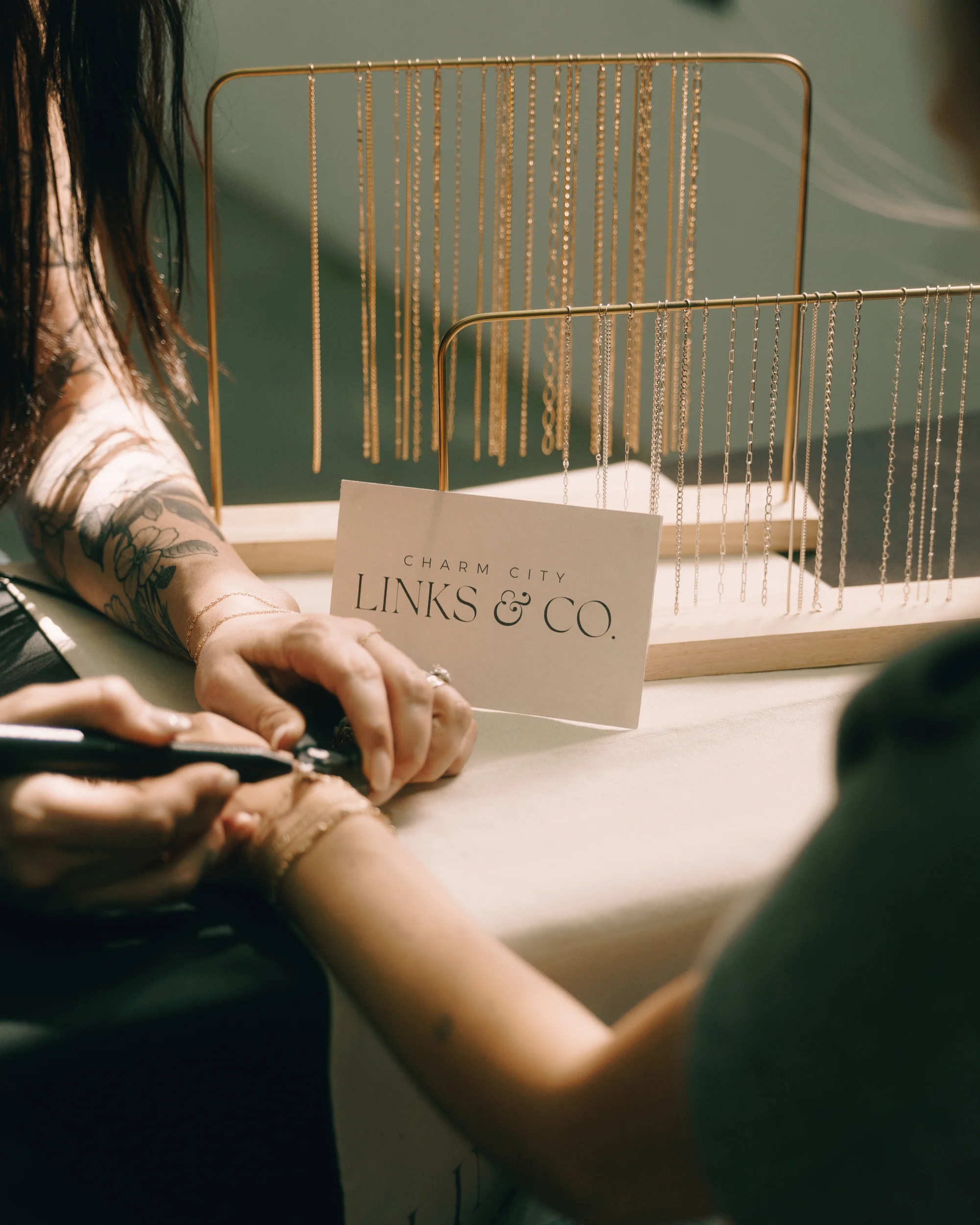 A chain being measured and cut to length on a customer's wrist, the brand card propped up beside the chain rack
