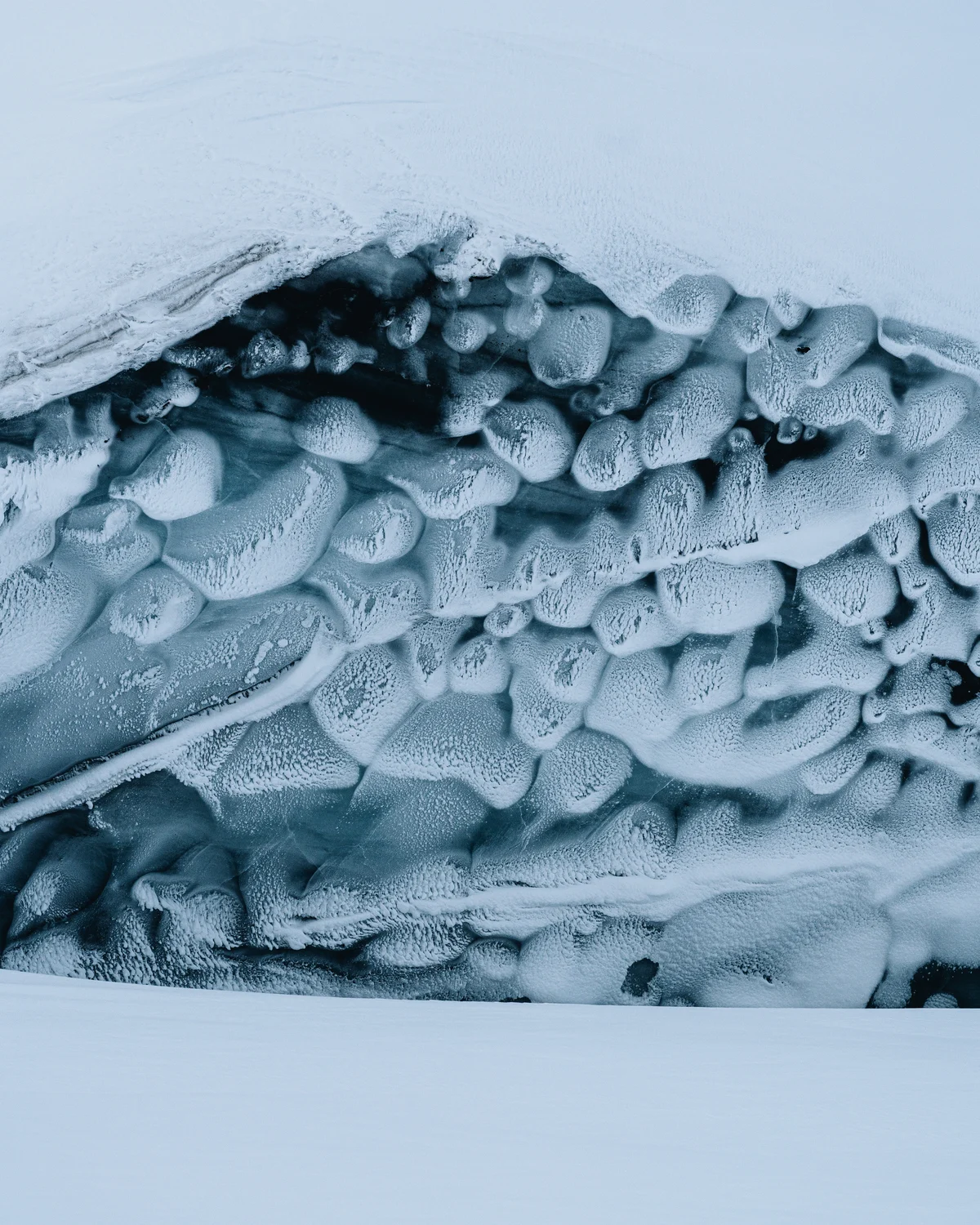 The wall of a glacier close up, lobed blue ice under a lip of wind-carved snow