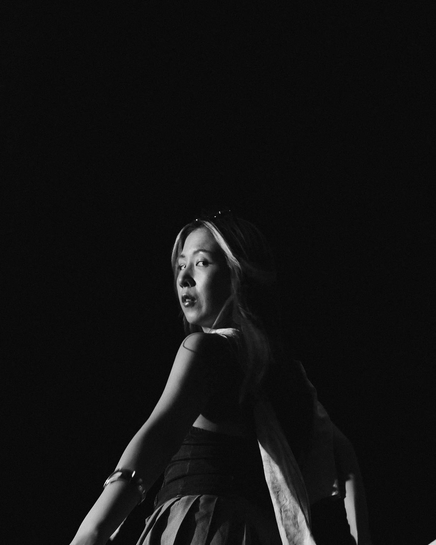 Black and white, looking back over a bare shoulder out of the dark