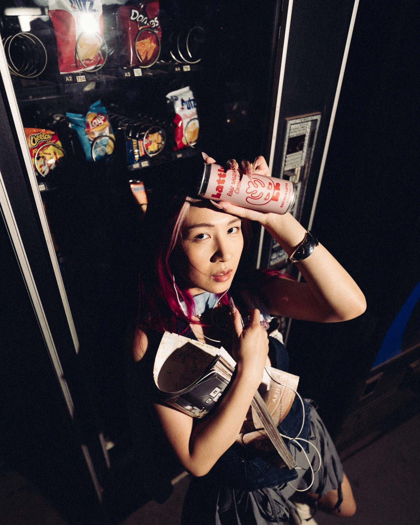 A can of Lattly held to her forehead in front of the vending machine