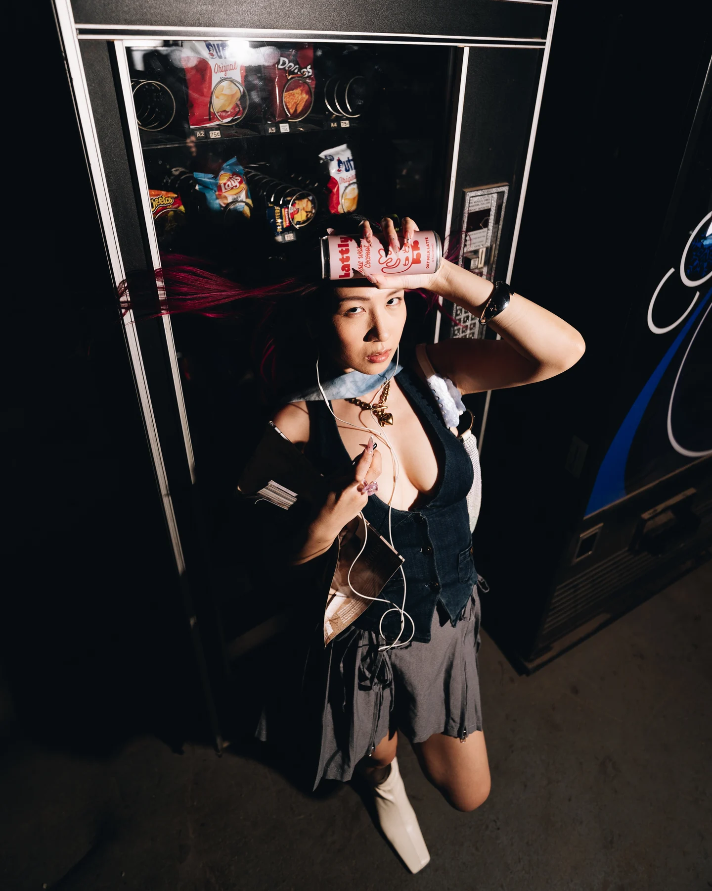 A hand raised to the head, headphone cords hanging, the vending machine glowing behind