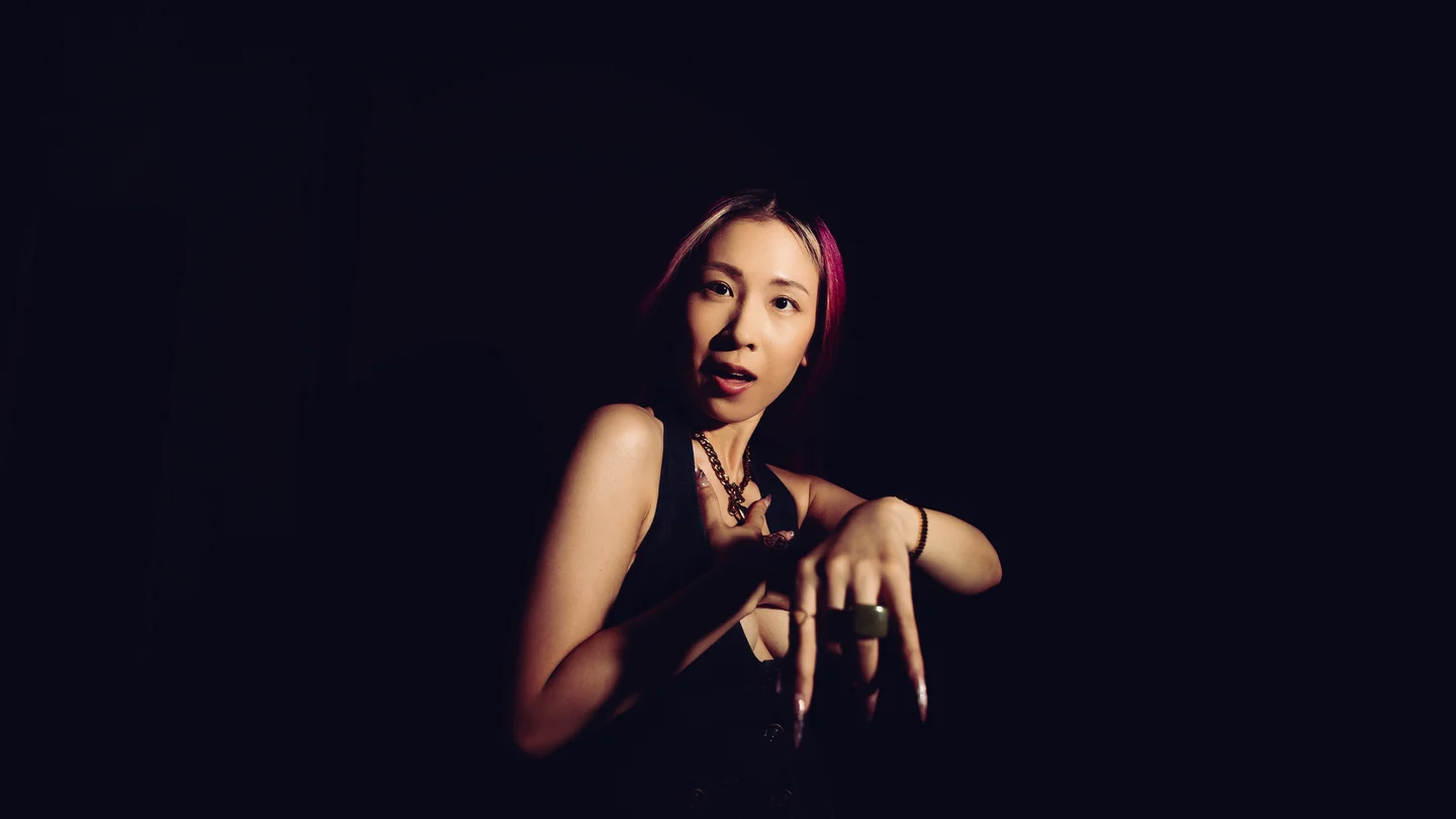 A small figure in the dark, lit from one side, hands raised to the face