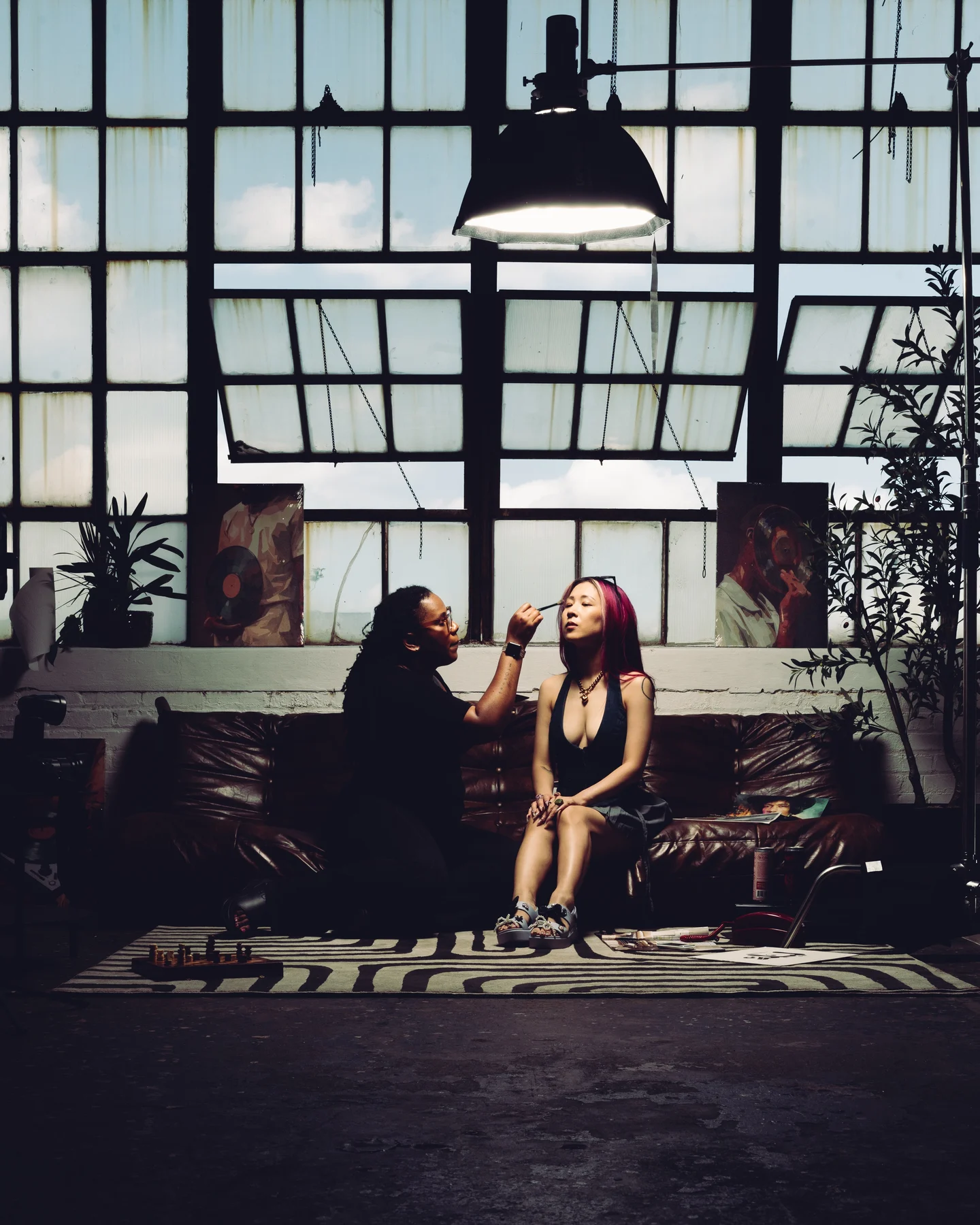 Two women sitting on the striped rug under the loft windows, one drinking from a can