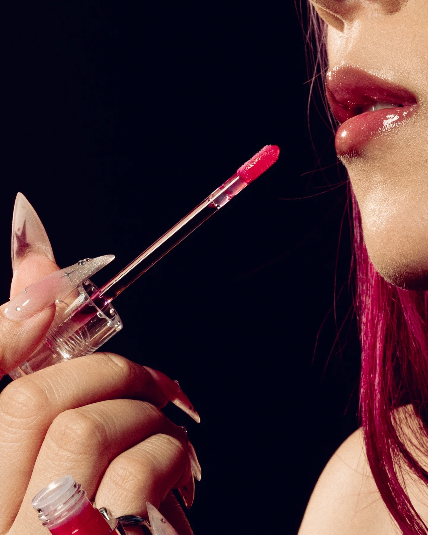 Close on a gloss wand at glossy lips, red tipped nails