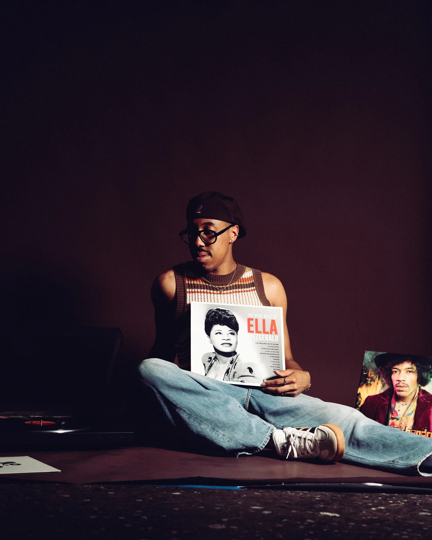 Kyle sitting cross legged on the sofa in headphones, holding an Ella record sleeve