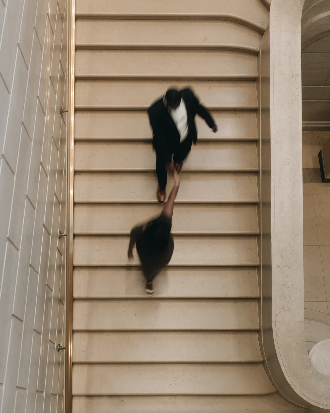 Looking straight down a curving stone staircase as a couple run up it, both blurred by the movement