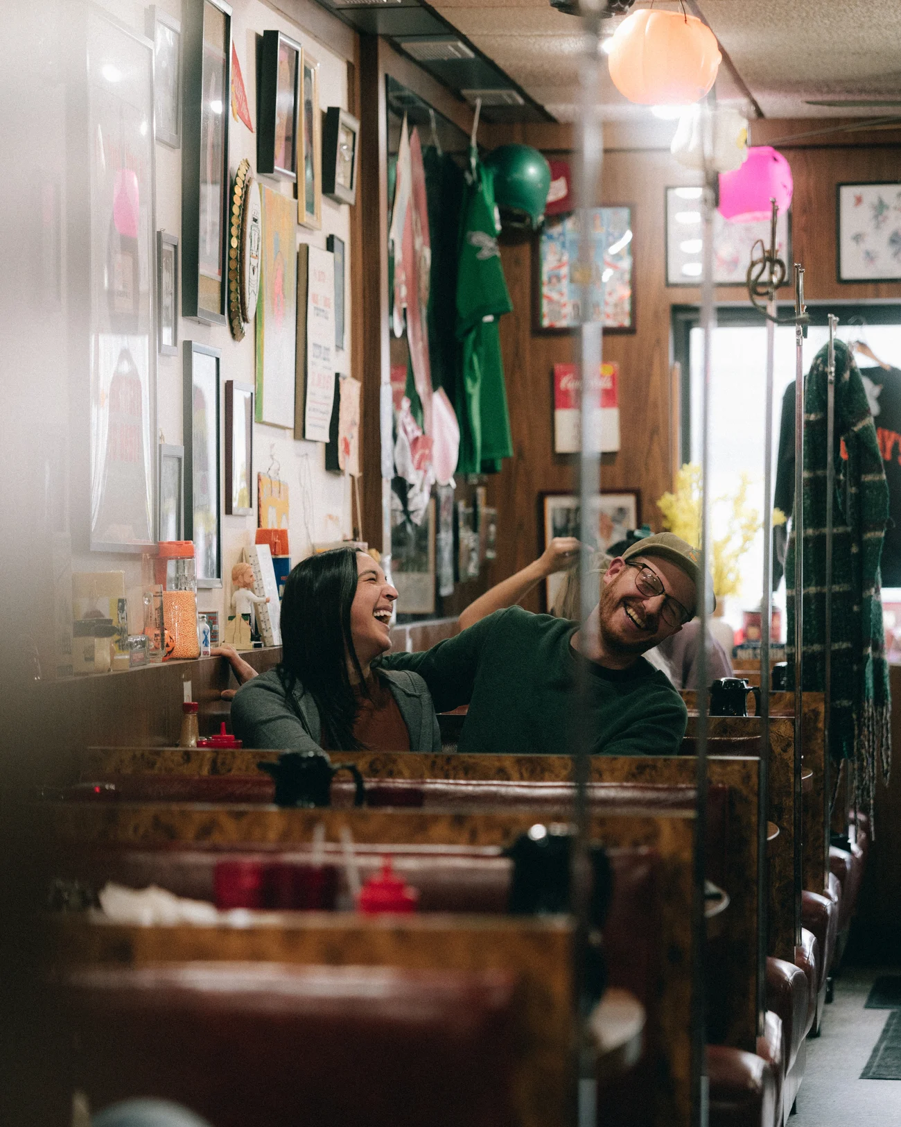 A couple laughing across the table of a diner booth, the walls behind them covered in framed pictures