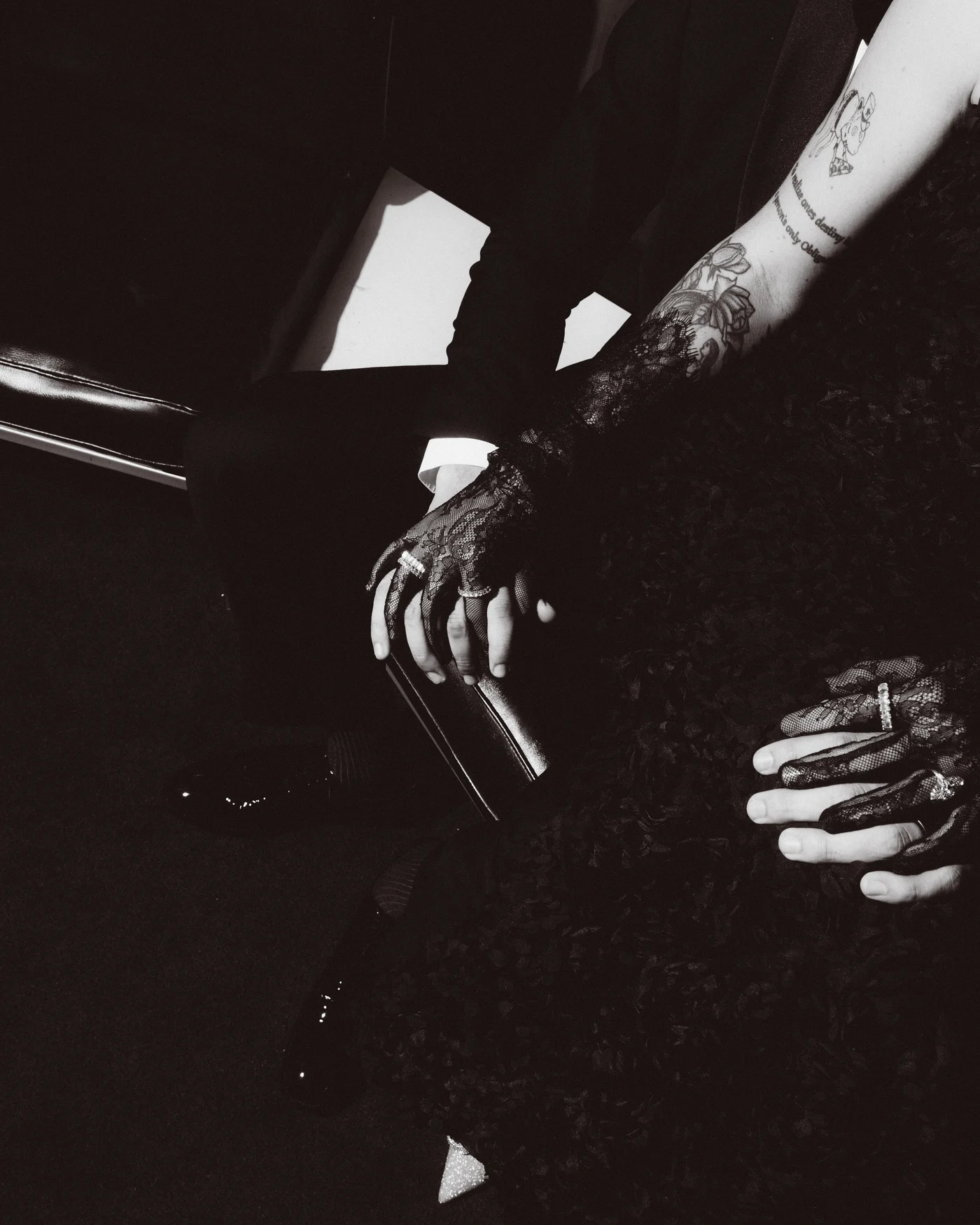 Two hands resting on a dark table in near darkness, one arm tattooed, a ring catching the last of the light