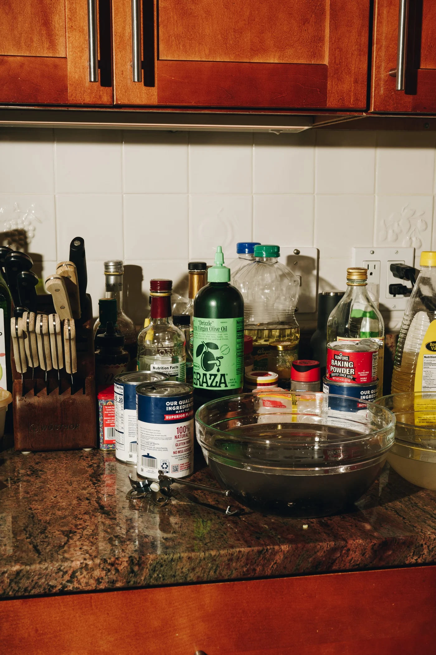 A counter crowded with oils, baking powder, and a glass bowl of soaking clams