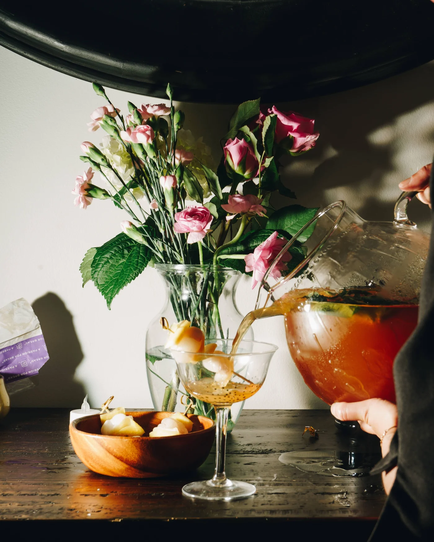 Punch pouring from a pitcher into a coupe beside a vase of garden roses