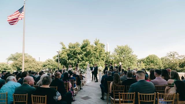 Guests seated for the outdoor ceremony beneath a tall flagpole, the couple exchanging vows at the far end of the terrace