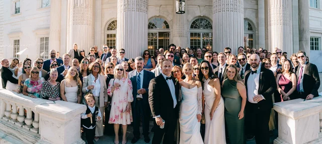 Panoramic portrait of the entire guest list gathered on the front steps around the couple