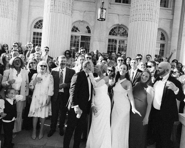 The couple kisses on the steps as the whole crowd of guests cheers around them