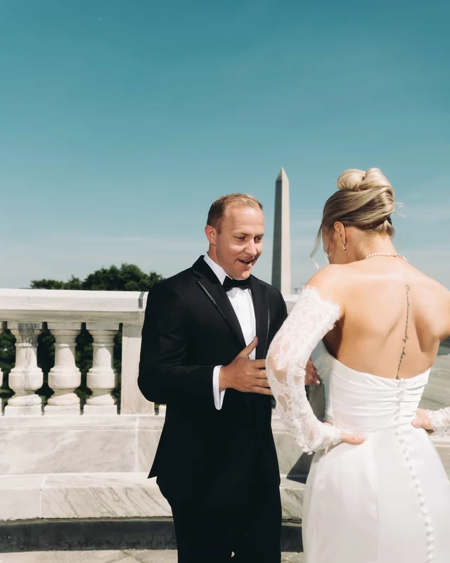 The groom turns and breaks into a grin at the first look, hand rising to his chest