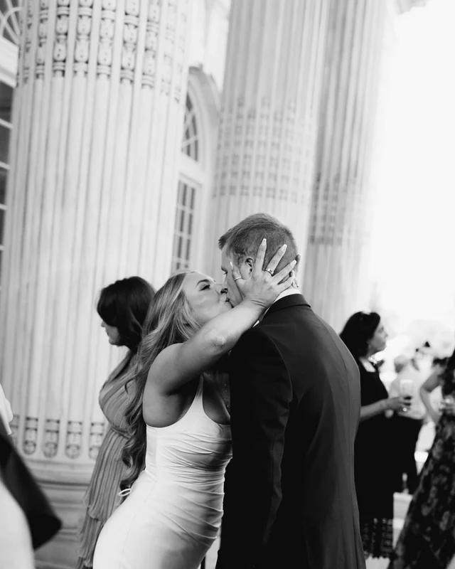 A long-haired guest pulls the groom in for a congratulatory kiss beside the fluted columns