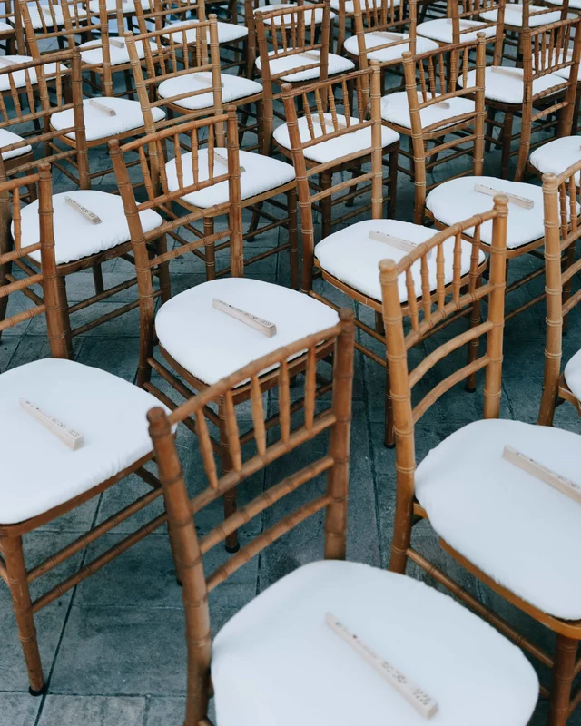 Rows of gold chiavari chairs with white cushions, a folded wooden fan resting on each seat