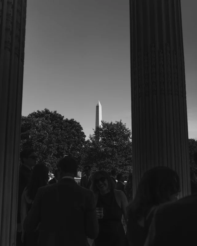 The monument framed between two dark column silhouettes above the treetops as guests mingle below