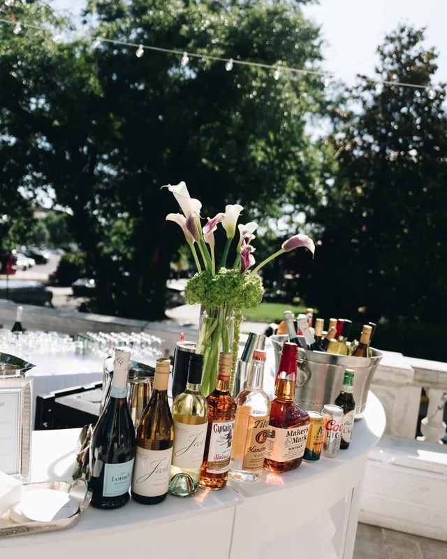 The outdoor bar lined with wine and whiskey bottles beside an ice bucket of beers and a calla lily arrangement