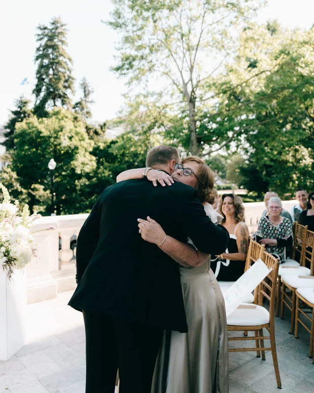 The groom wraps a woman in glasses in a long hug at the head of the aisle