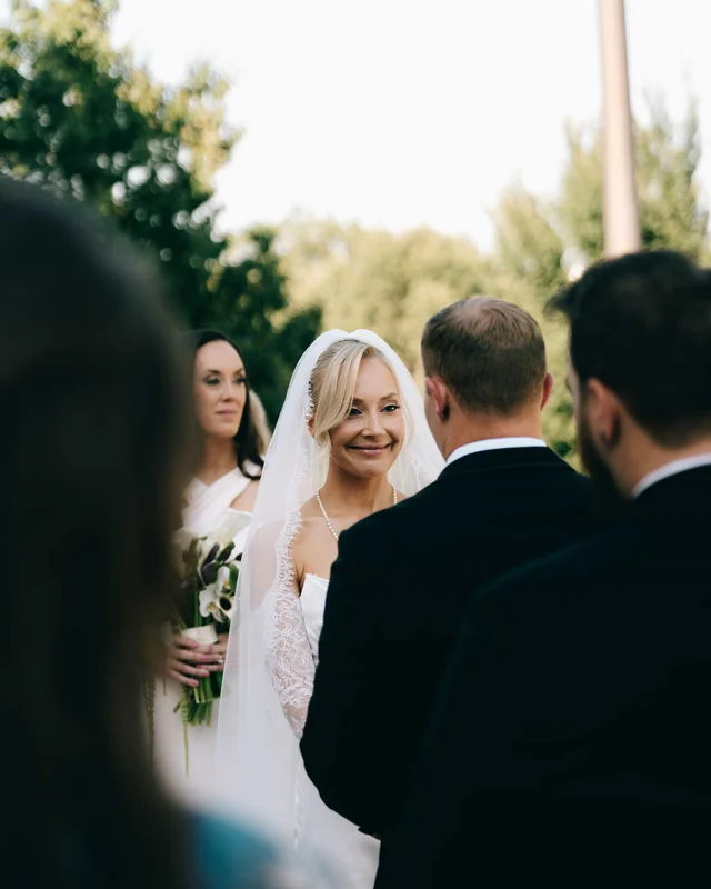 The bride's soft smile at the groom during the ceremony, veil framing her face, greenery glowing behind