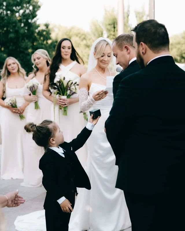 The ring bearer stretches up on tiptoe to deliver the black ring box mid-ceremony